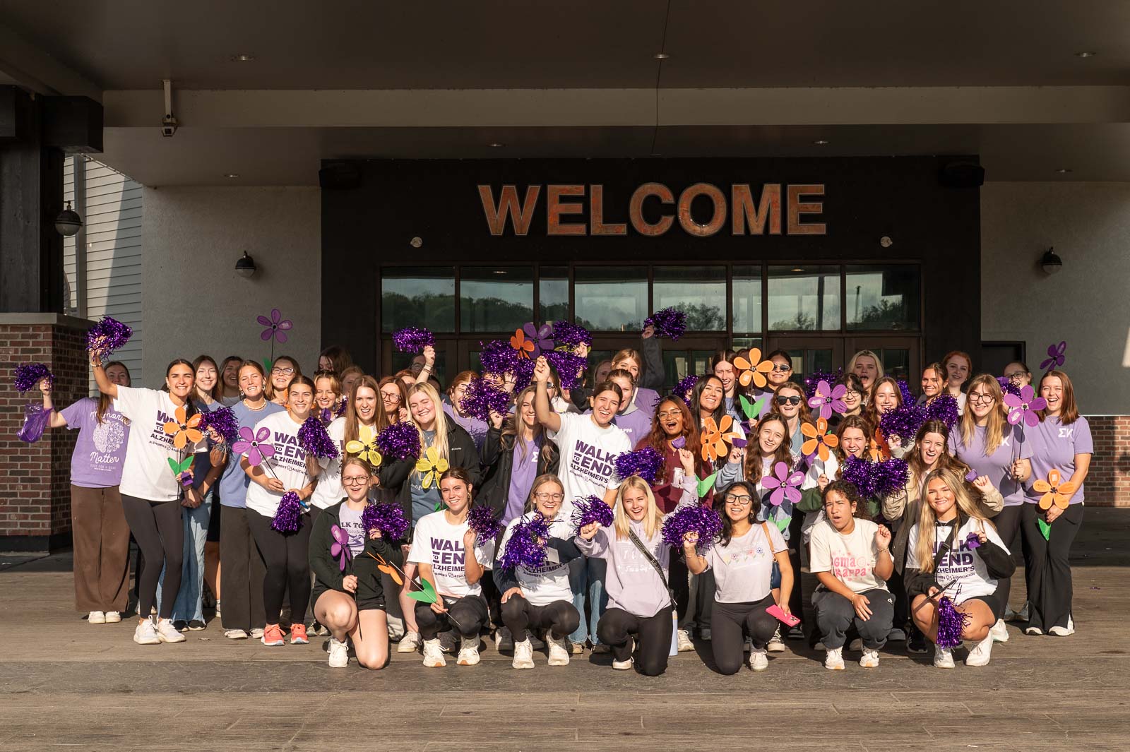 Large group of participants holding purple flowers and pom-poms under the Welcome sign at the Walk to End Alzheimer’s in St. Joseph, Missouri.